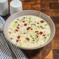 Creamy soup with green onions and crispy bacon bits in a beige bowl.