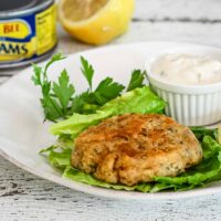 Clam cake on a plate with lettuce, tartar sauce, and a lemon half.