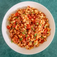 Greased pasta with ground beef and tomato sauce in a white bowl.