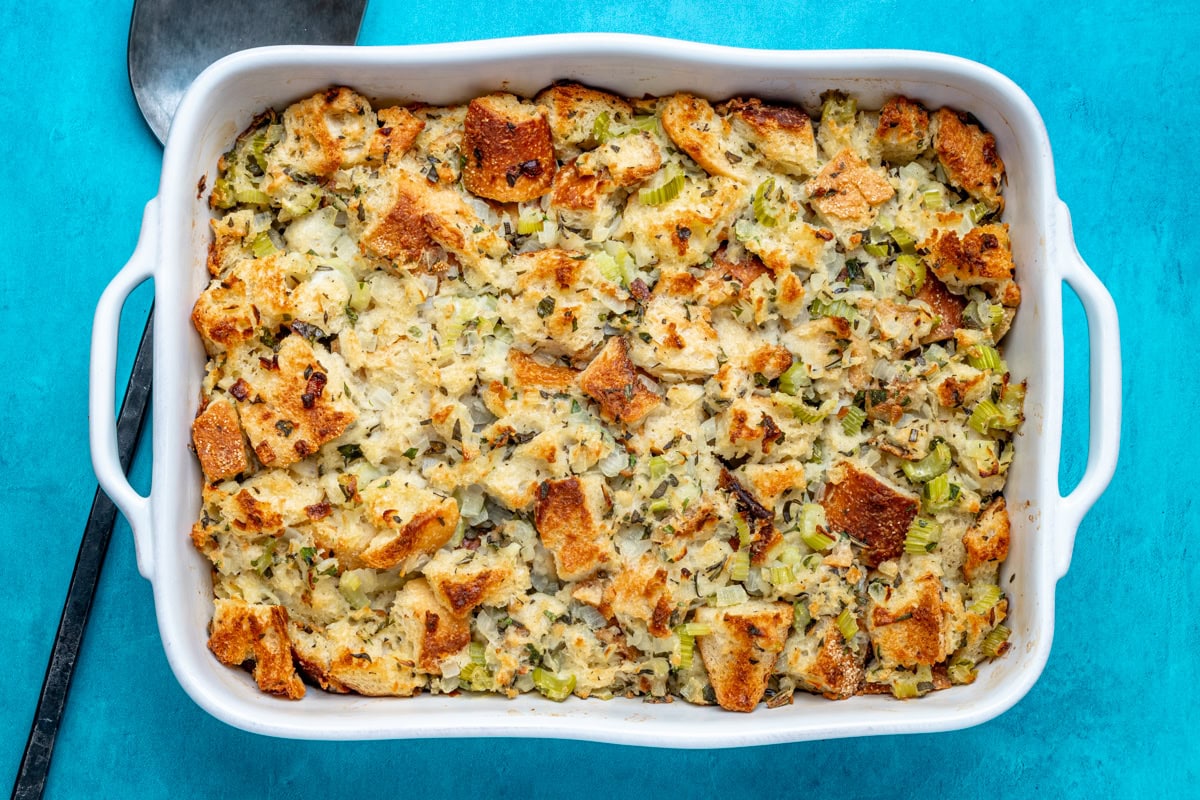 A baking dish with bread stuffing with a serving spoon on the side.