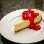 a slice of classic cheesecake on a plate with a garnish of cherry pie filling