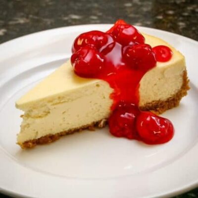 A slice of classic cheesecake with a garnish of cherry pie filling