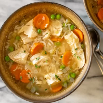 Creamy chicken and vegetable rice soup in a rustic bowl, with carrots, peas, and shredded chicken.