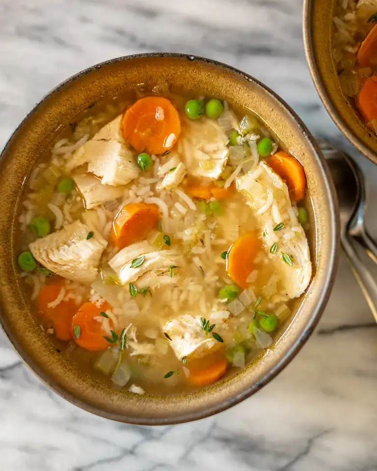 Creamy chicken and vegetable rice soup in a rustic bowl, with carrots, peas, and shredded chicken.