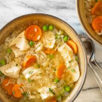 A bowl of chicken and rice soup with carrots, peas, and fresh thyme leaves for garnish.