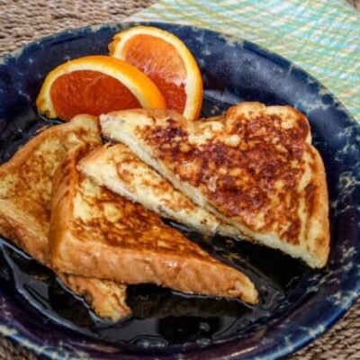 sliced French toast on a plate with orange wedges on the side.
