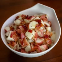 Crispy bacon and diced boiled eggs in a white bowl on a wooden table.