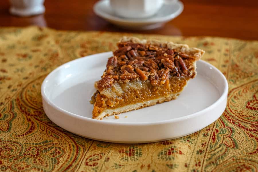 A layered pumpkin pie with pecan pie topping on a plate.

