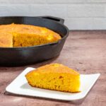 american cornbread slice on a plate with iron skillet in the background