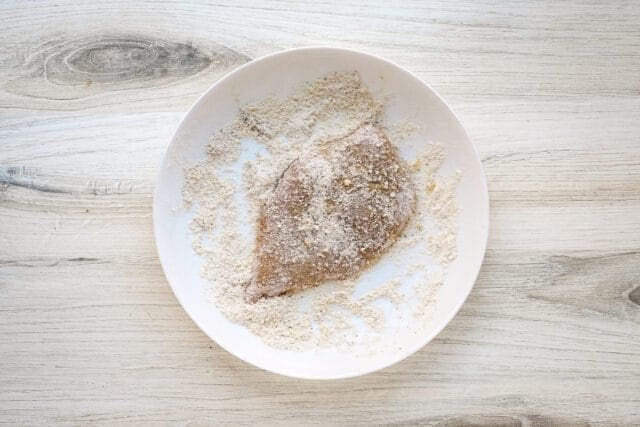 Lightly coated fish fillet on a white plate surrounded by breadcrumbs.