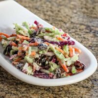 Colorful coleslaw with green and red cabbage, celery, carrots, and raisins, in a small dish.