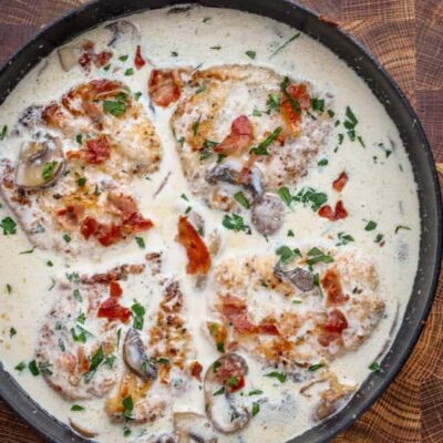 Cooked chicken breasts in a creamy wine sauce garnished with parsley and crispy prosciutto.