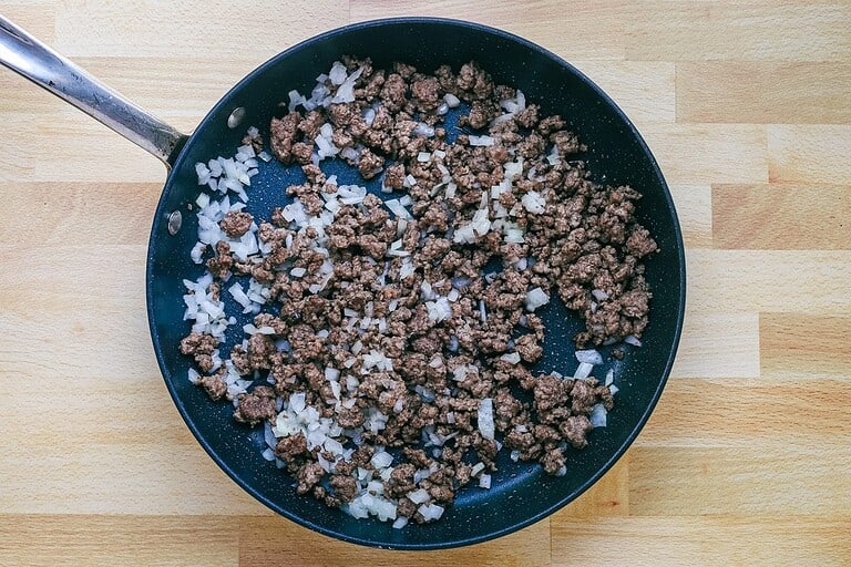 Cooked ground beef with chopped onions in a black skillet.