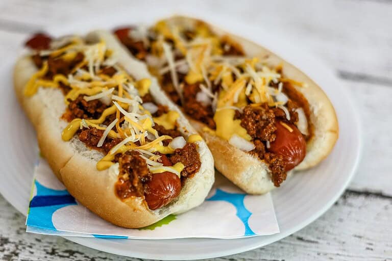 Hot dog with chili, shredded cheese, and mustard on a white plate.
