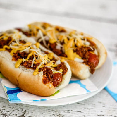 Hot dog with chili, shredded cheese, and mustard on a bun.