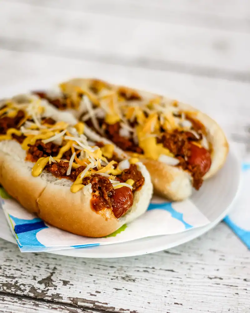 Hot dog with chili, shredded cheese, and mustard on a bun.