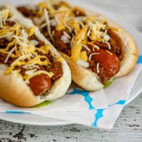 Hot dogs with chili, shredded cheese, and mustard on buns.