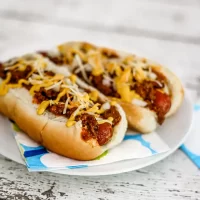 Hot dogs with chili, shredded cheese, and mustard on a bun.