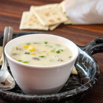 Creamy corn and green onion soup in a white bowl with naan bread on the side.