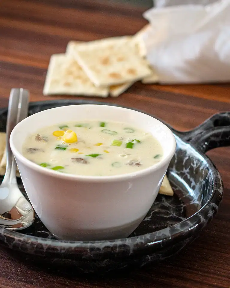 Creamy corn and green onion soup in a white bowl with naan bread on the side.