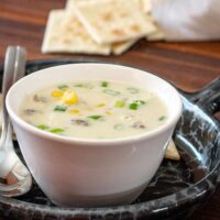 A cup of corn and bacon chowder with saltines.