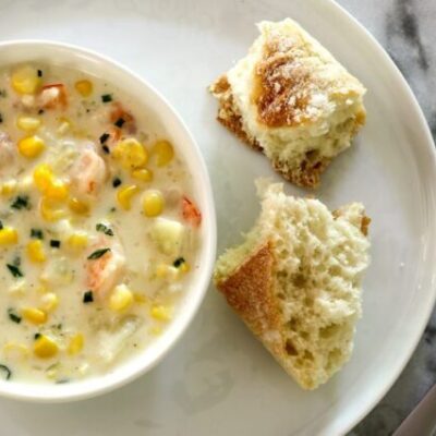 corn and shrimp chowder in a bowl with bread and chives for garnish