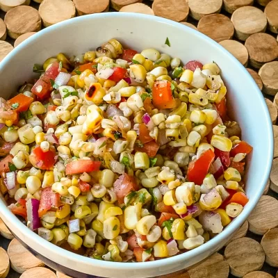 Fresh corn salad mixed with chopped tomatoes, onions, and herbs in a white bowl.