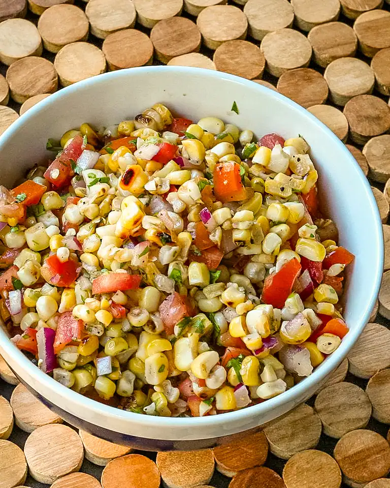 Fresh corn salad mixed with chopped tomatoes, onions, and herbs in a white bowl.