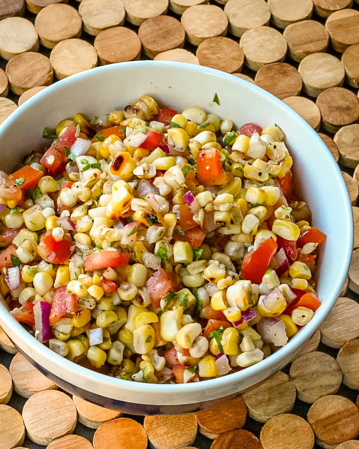 Fresh corn salad mixed with chopped tomatoes, onions, and herbs in a white bowl.