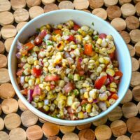 A serving bowl of corn salsa with charred corn, diced tomatoes, cilantro, red onion, and peppers.