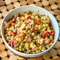 Fresh corn and vegetable salad in bowl with chopped herbs.