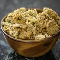 Seasoned breaded chicken pieces in a small brown bowl on dark surface.