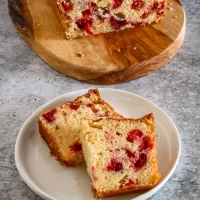 Moist cherry cake with a white glaze topping on a wooden cutting board.