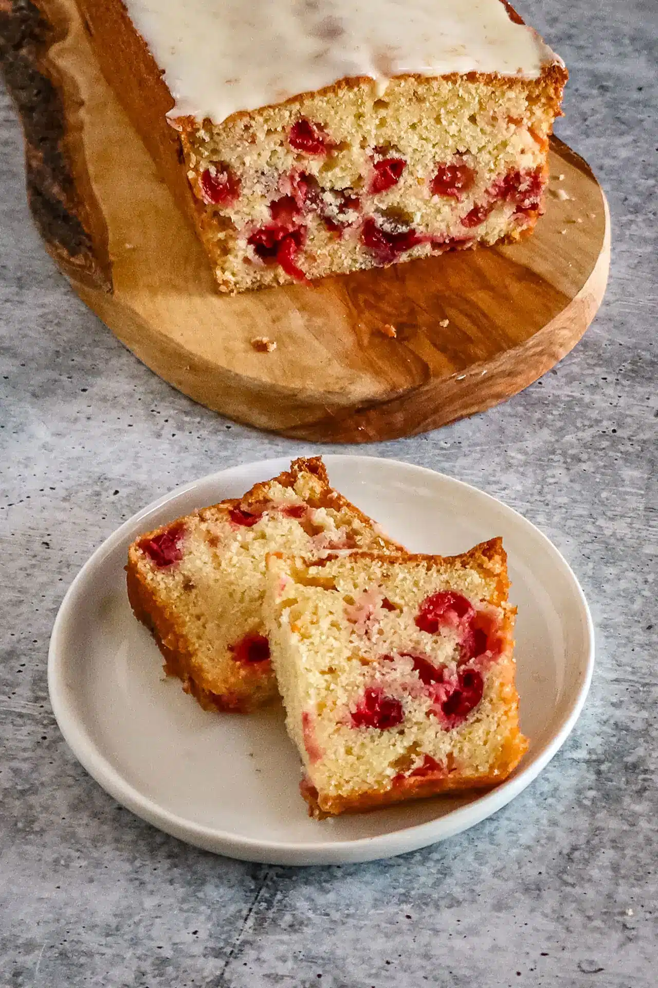 Moist cherry cake with a white glaze topping on a wooden cutting board.