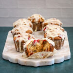 Cranberry orange muffins with glaze and one muffin split to show interior texture and color.