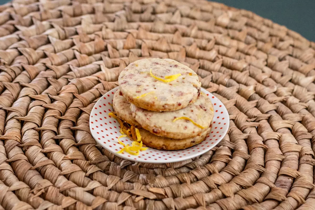 Golden lemon-flavored cookies with lemon zest on plate over woven surface.