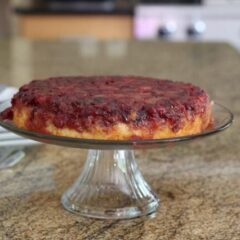 cranberry upside-down cake on a cake stand with plates for serving
