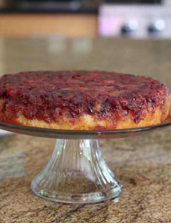 cranberry upside-down cake on a cake stand with plates for serving