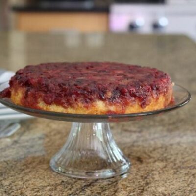 cranberry upside-down cake on a cake stand with plates for serving