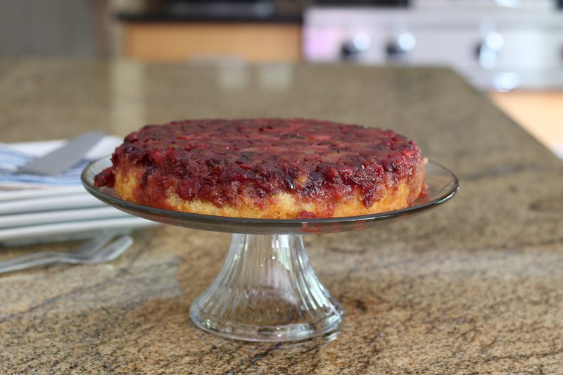 cranberry upside-down cake on a cake stand with plates for serving