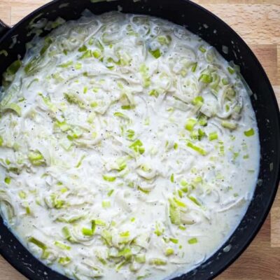 Creamy leek and garlic sauce in a black skillet on a wooden surface.