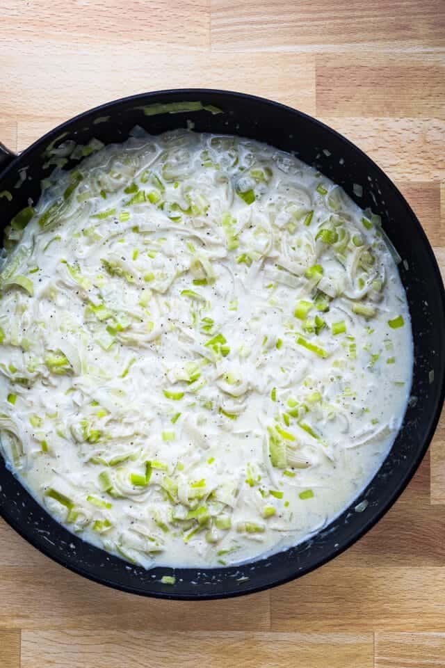 Creamy leek and garlic sauce in a black skillet on a wooden surface.