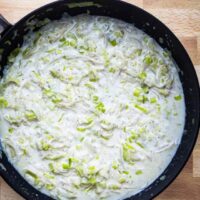 Creamy leek and garlic sauce simmering in a black skillet.