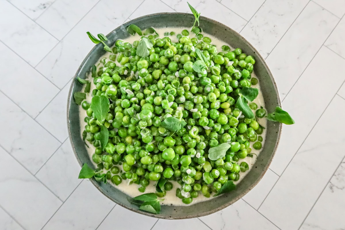 Creamed peas in a serving bowl with pea shoots.