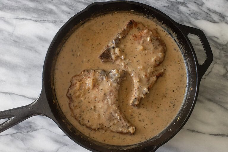 Chunks of meat cooking in creamy, seasoned sauce in a black skillet.
