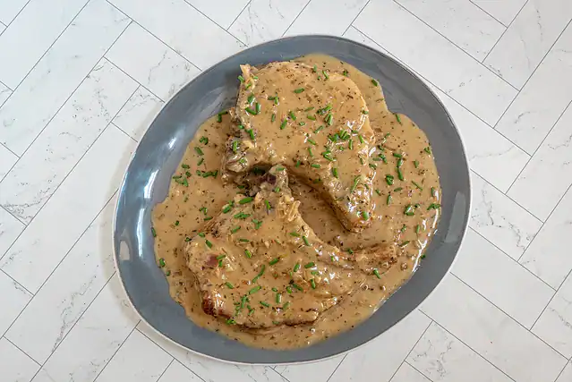 A plate with creamy apple cider pork chops and sauce, garnished with chives.