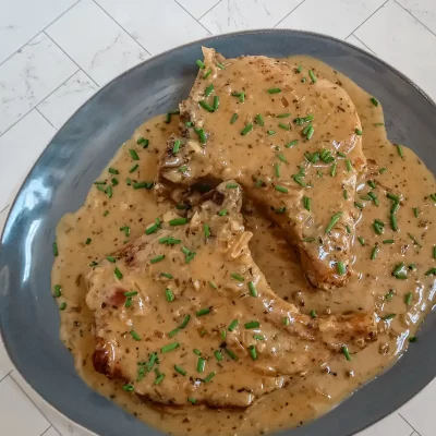 Creamy gravy-covered meat served on a blue plate garnished with chopped chives.