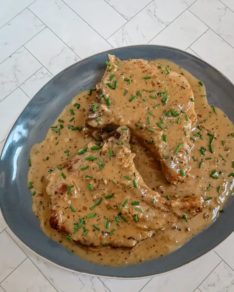 Creamy gravy-covered meat served on a blue plate garnished with chopped chives.