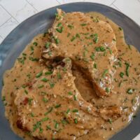 A plate with creamy apple cider pork chops and sauce, garnished with chives.