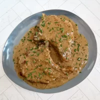 Creamy gravy with two cooked meat pieces garnished with chopped chives.
